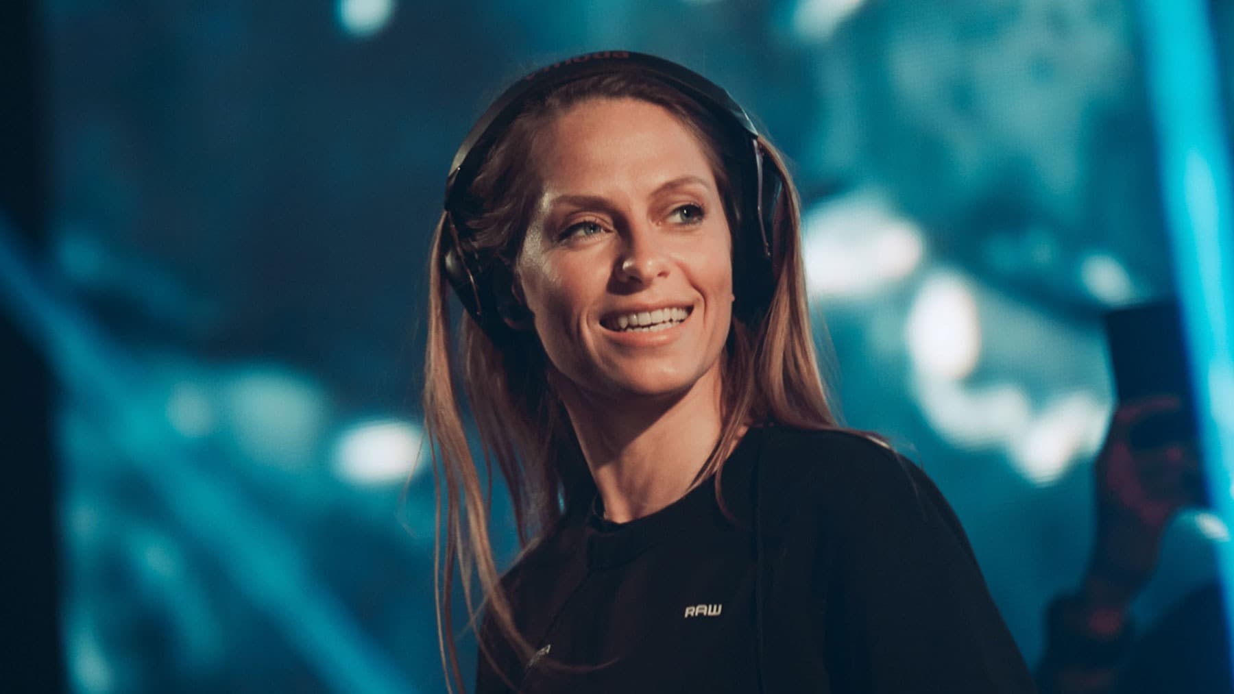 Nora En Pure у навушниках усміхається на тлі синього екрана