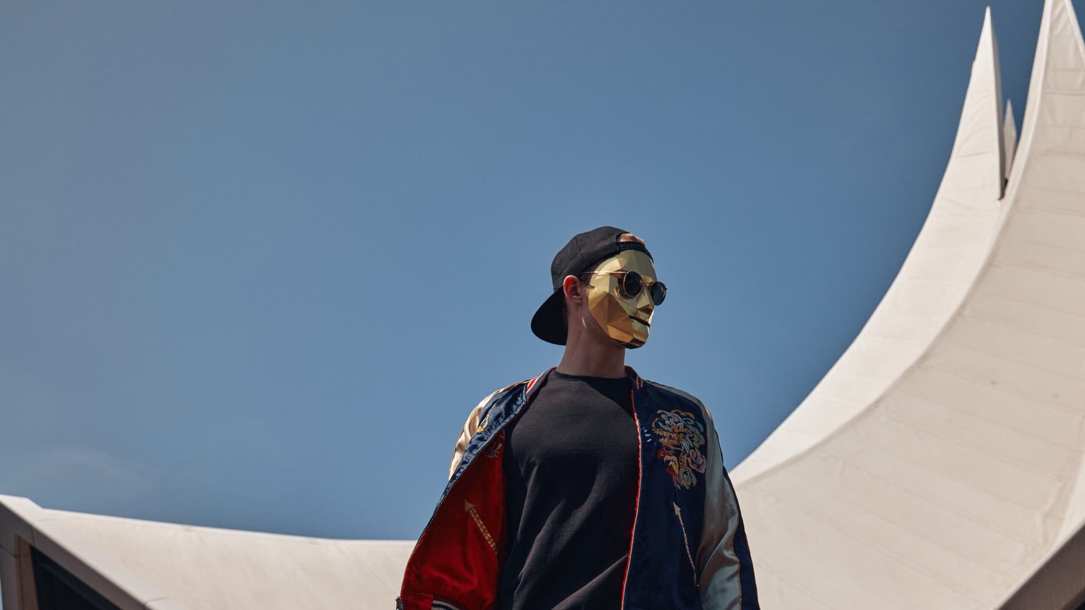 Satin Jackets in a gold mask, cap and jacket against the sky